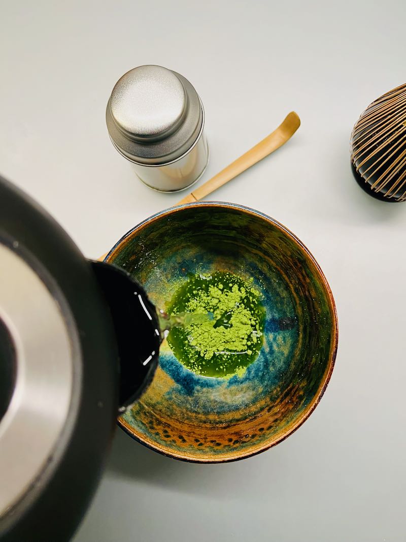 Little hot water over the matcha powder. With a kettle, a little hot water is poured onto the matcha powder.