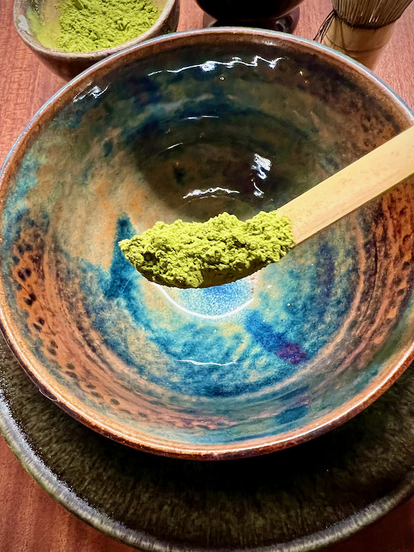 Matcha on a bamboo spoon. Matcha on a bamboo spoon. At the back an empty bowl.